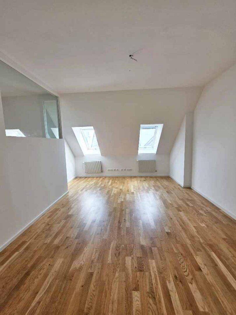 Großes, helles Zimmer im Dachgeschoss mit Holzparkettboden und zwei Dachfenstern, ideal als Schlafzimmer.