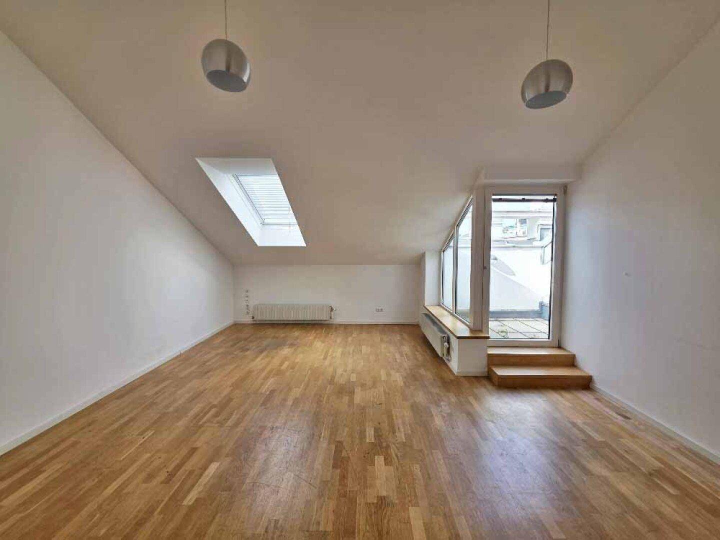 Heller Wohnbereich im Dachgeschoss mit Holzparkettboden, Dachfenster und Zugang zu einer Außenterrasse.