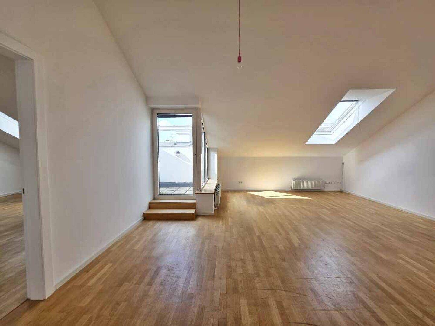 Geräumiger Wohnbereich im Dachgeschoss mit Holzparkettboden, Dachfenstern und Zugang zu einer Terrasse.