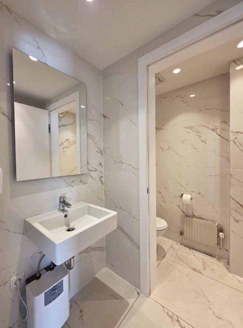 Modernes Badezimmer mit weißen Marmorfliesen, wandmontiertem Waschbecken und integrierter Beleuchtung.
