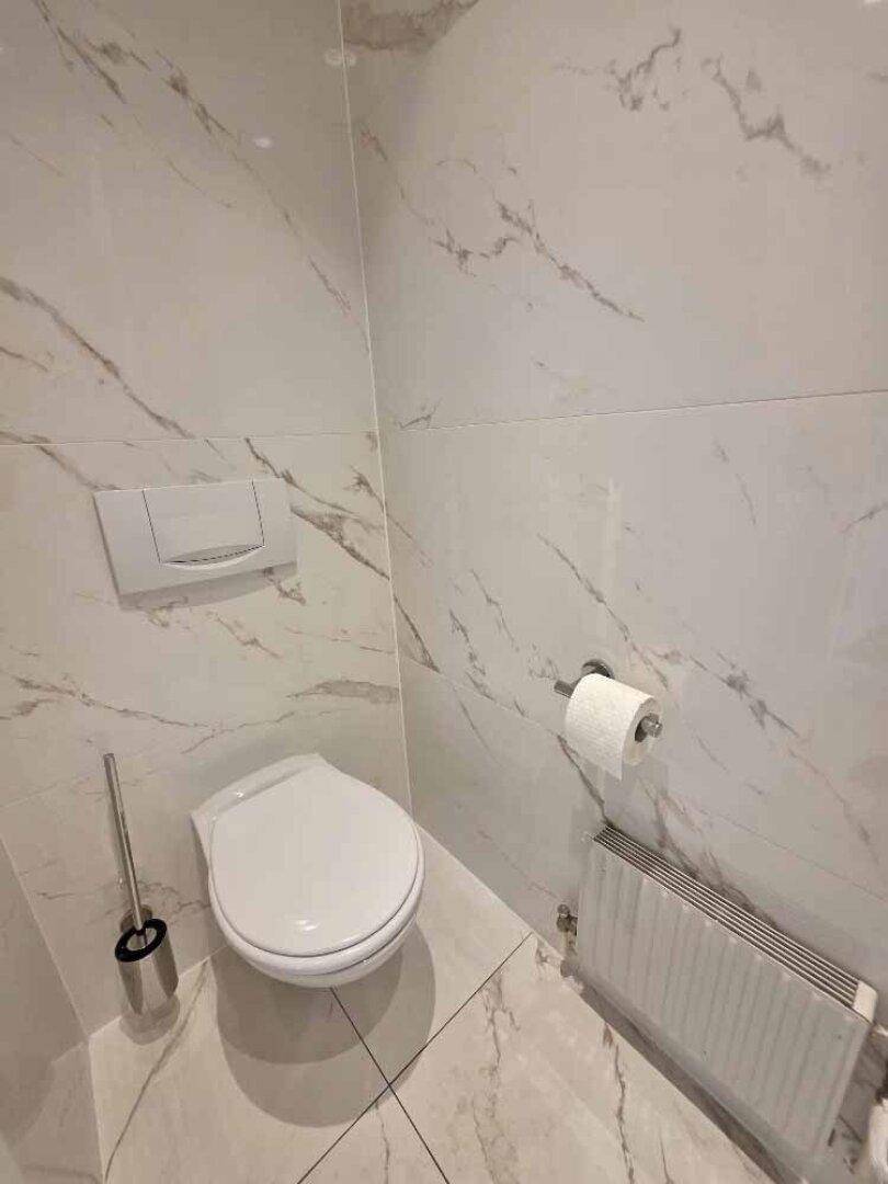 Separate Toilette mit modernen weißen Marmorfliesen, wandhängendem WC und Heizkörper.