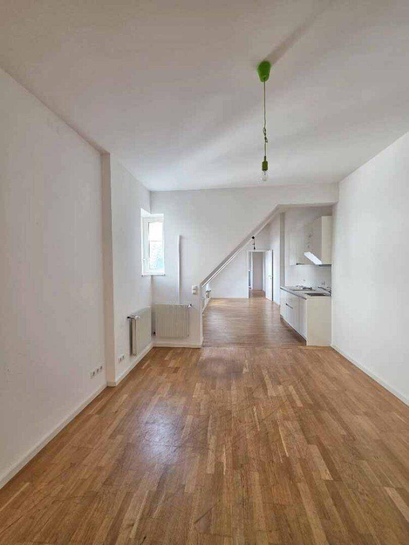 Offener Wohnbereich mit integrierter Küchenzeile, Holzparkettboden und einem Fenster mit Blick nach draußen.
