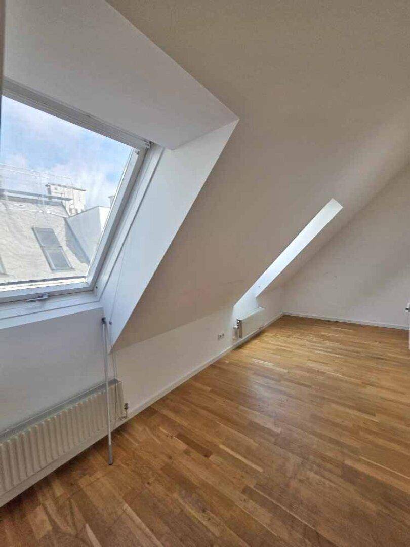 Helles Zimmer im Dachgeschoss mit Holzparkettboden und einem großen Dachfenster, das viel Licht hereinlässt.