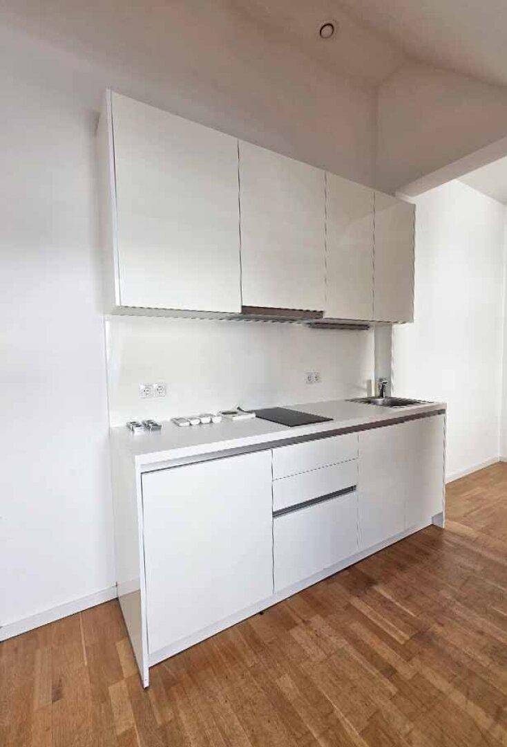 Moderne, weiße Küchenzeile mit glänzenden Oberschränken, integriertem Kochfeld und Spüle.