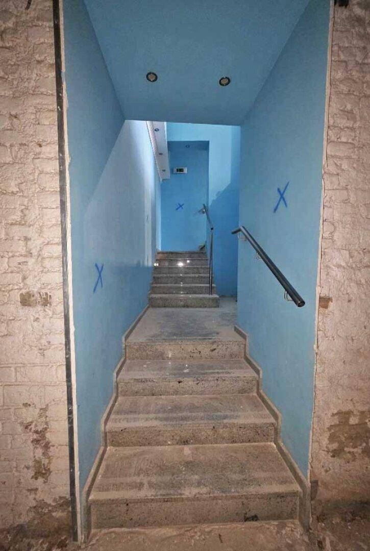 Treppenhaus mit blauen Wänden und Steinstufen, das in ein Untergeschoss führt, mit einem einfachen Handlauf.