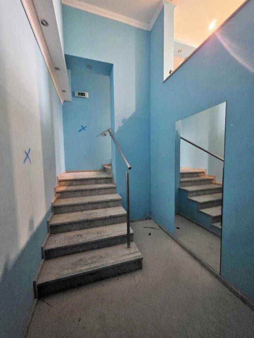 Treppenhausbereich mit blauen Wänden, Steinstufen und einem großen Spiegel, der die Treppe reflektiert.