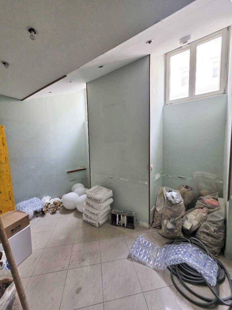 Renovierungsbedürftiger Raum mit hellblauen Wänden, Fliesenboden und Baumaterialien, beleuchtet durch ein Fenster.