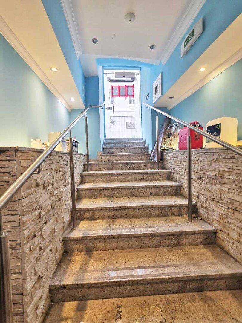 Innenansicht eines Treppenhauses mit blauen Wänden, Steinstufen und einem modernen Edelstahlgeländer.
