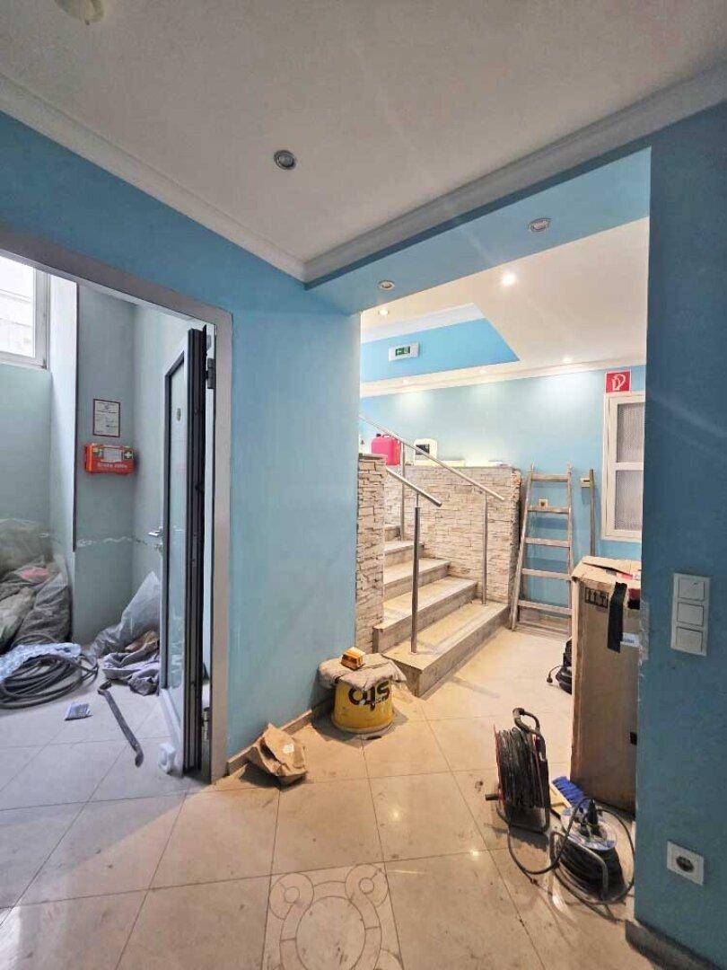 Flur mit blauen Wänden und Fliesenboden, der zu einem Treppenhaus führt, mit einigen Baumaterialien.