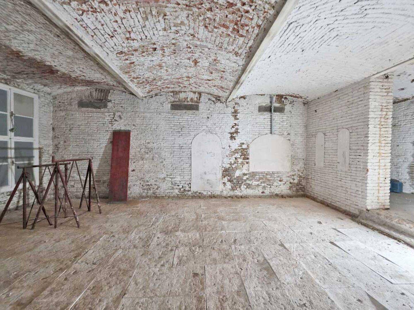 Ansicht des rohen Kellerraums mit freiliegenden Ziegelwänden, Gewölbedecke und einem groben Holzboden.