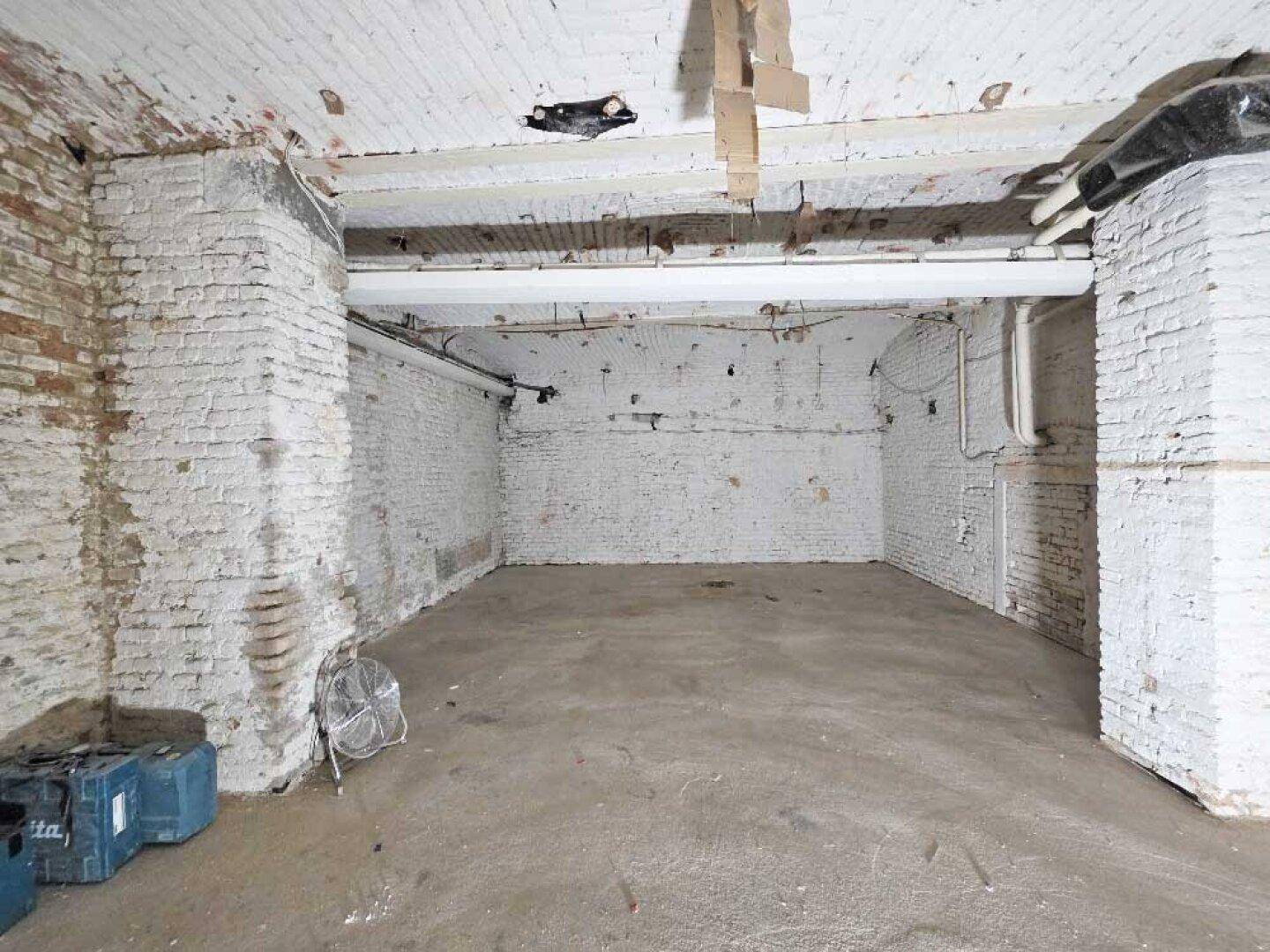 Ecke eines großen Kellerraums mit freiliegenden Ziegelwänden, Betonboden und sichtbaren Installationen.