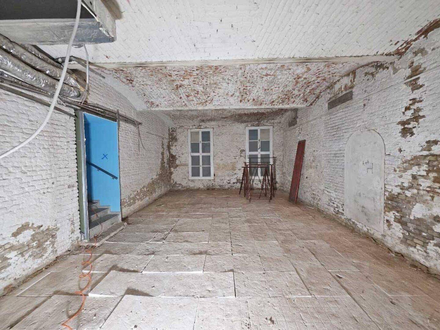 Weiterer Blick in den großen Kellerraum mit zwei Fenstern, freiliegenden Ziegelwänden und einer Gewölbedecke.
