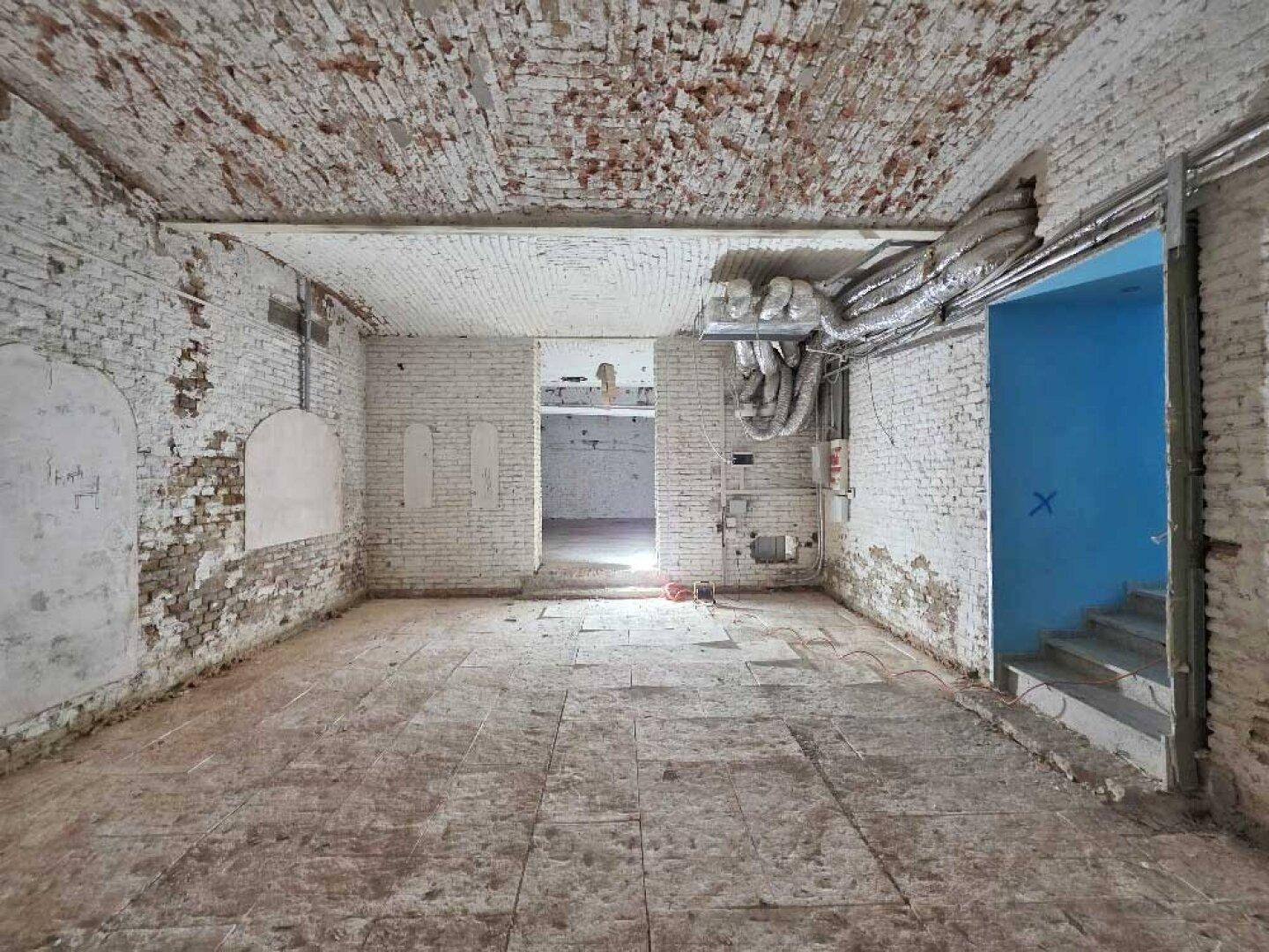Großer, roher Kellerraum mit freiliegenden Ziegelwänden und -decke sowie einem Zugang zu einem Treppenhaus.