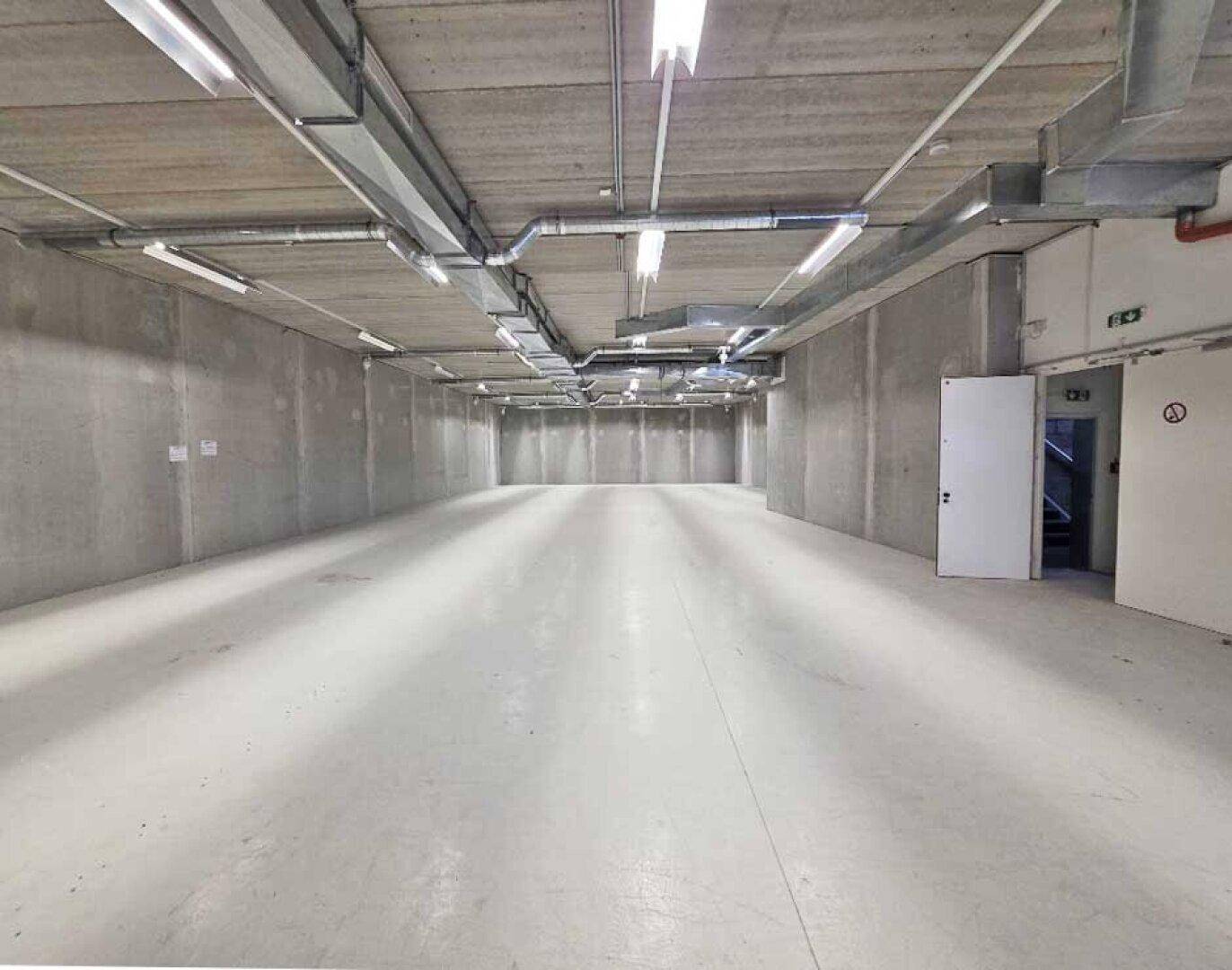 Langer, heller Kellerraum mit Betonwänden und -boden, ausgestattet mit moderner Beleuchtung.