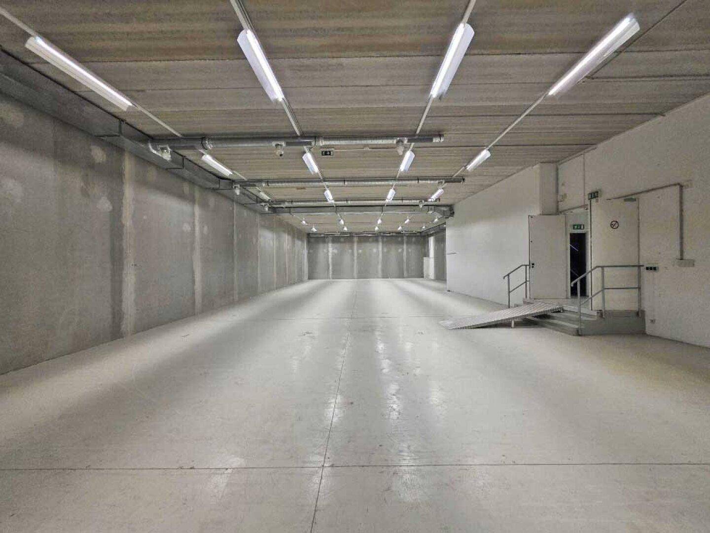 Langer, heller Kellerraum mit Betonwänden und -boden, ausgestattet mit moderner Beleuchtung.