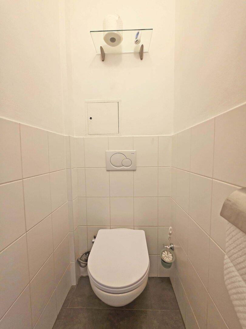 Separates WC mit Wand-WC und weißen Fliesen.