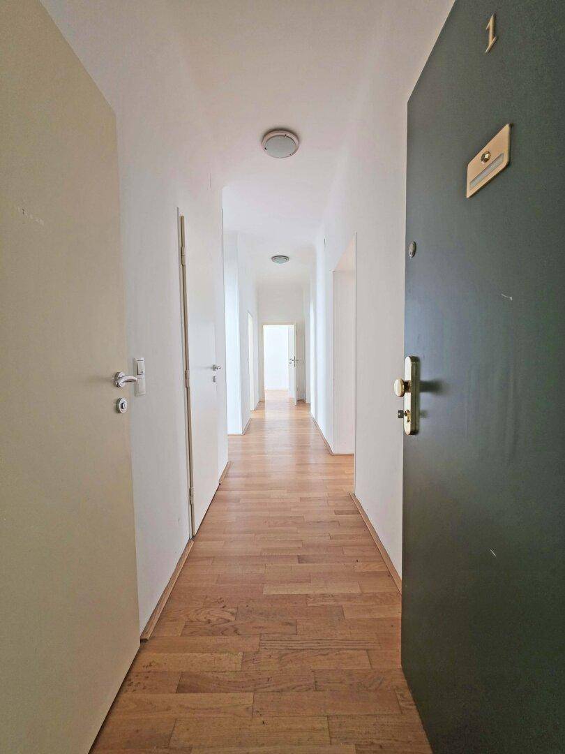 Langer, heller Flur mit Holzboden und mehreren Türen.
