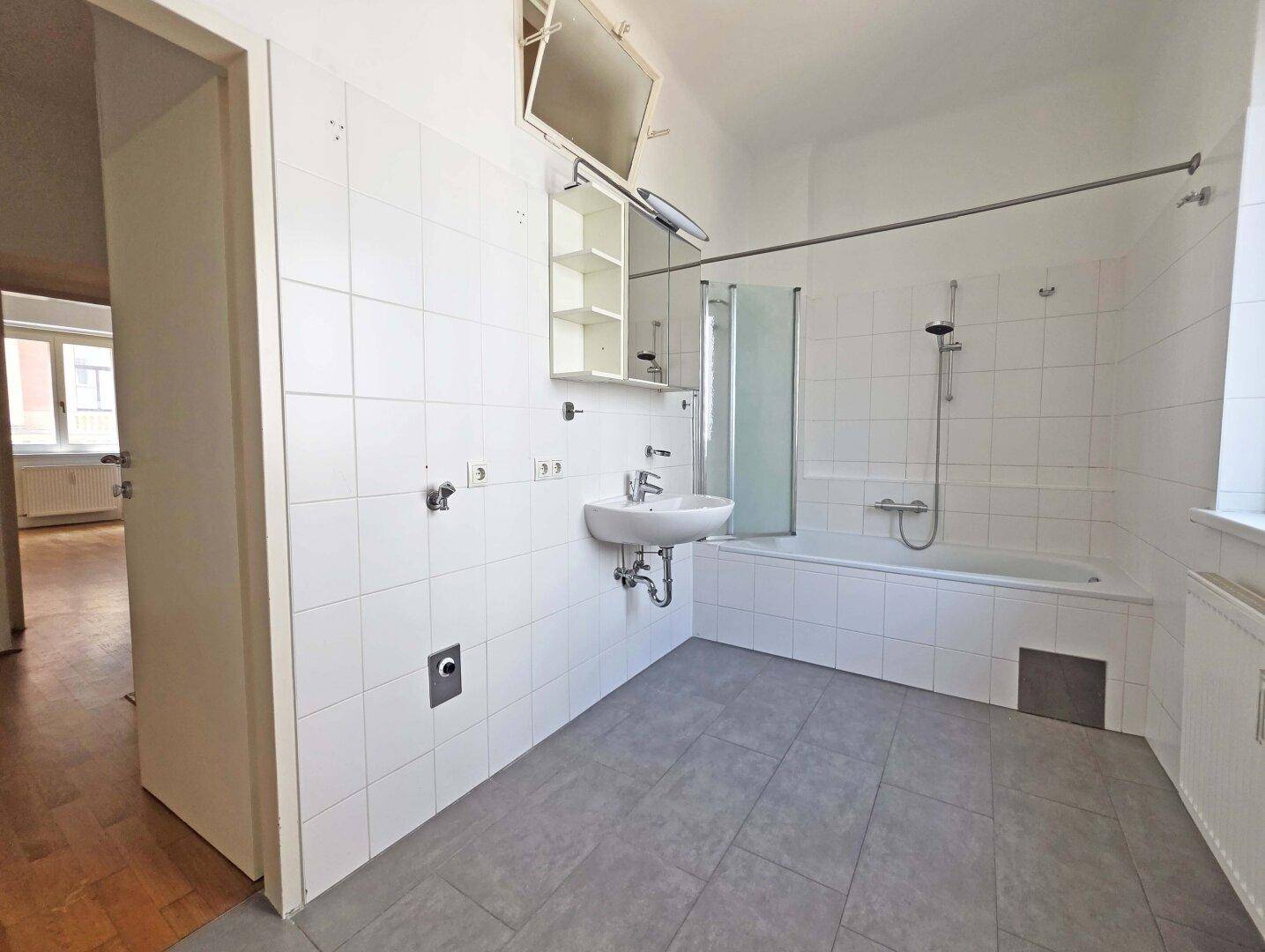 Helles Badezimmer mit weißen Fliesen, Badewanne und Waschbecken.