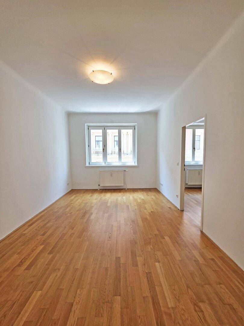 Helles Zimmer mit Holzboden und einem großen Fenster, bereit zur Einrichtung.