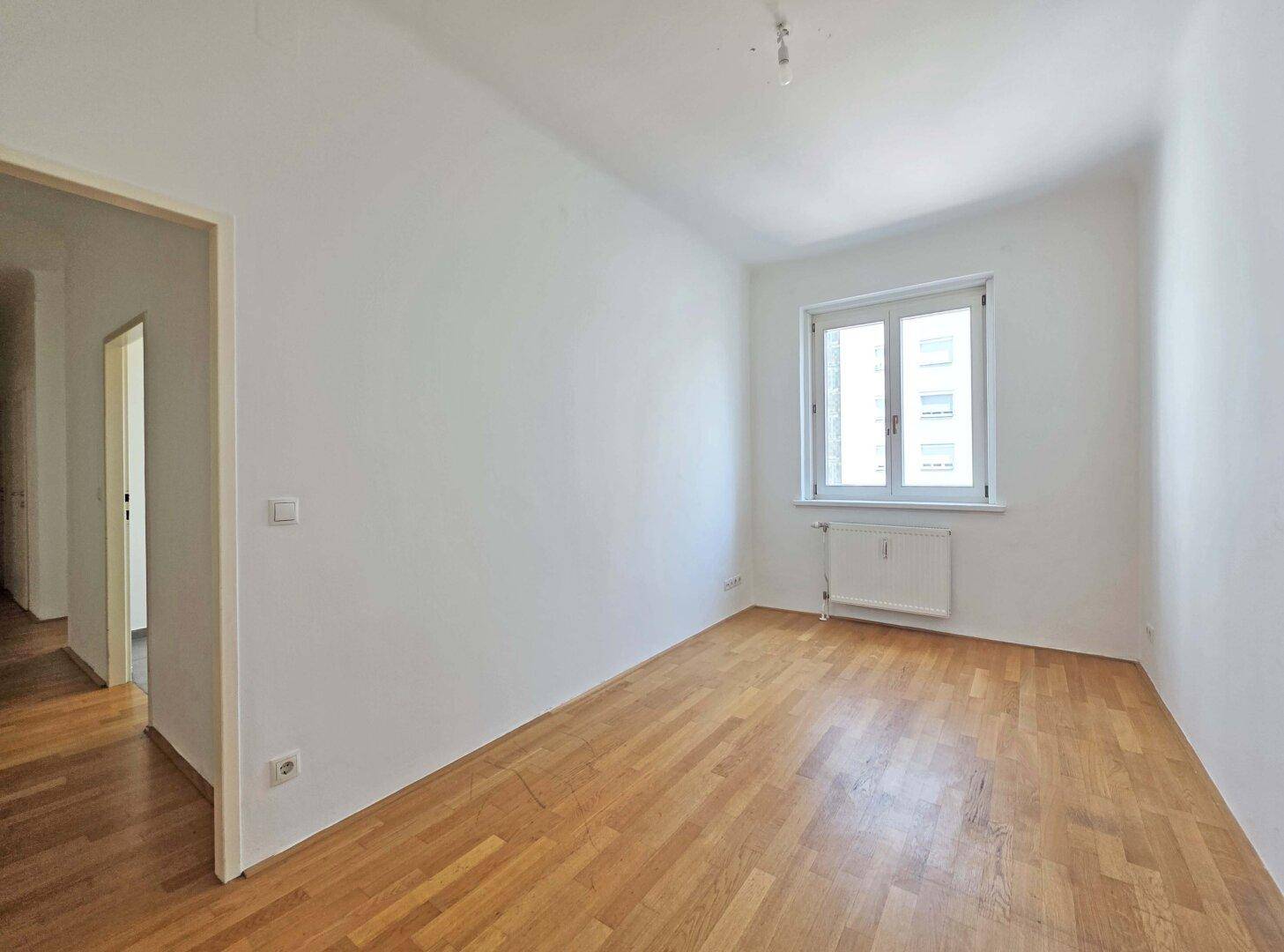 Kleineres Zimmer mit Holzboden und einem Fenster, ideal als Schlaf- oder Arbeitszimmer.