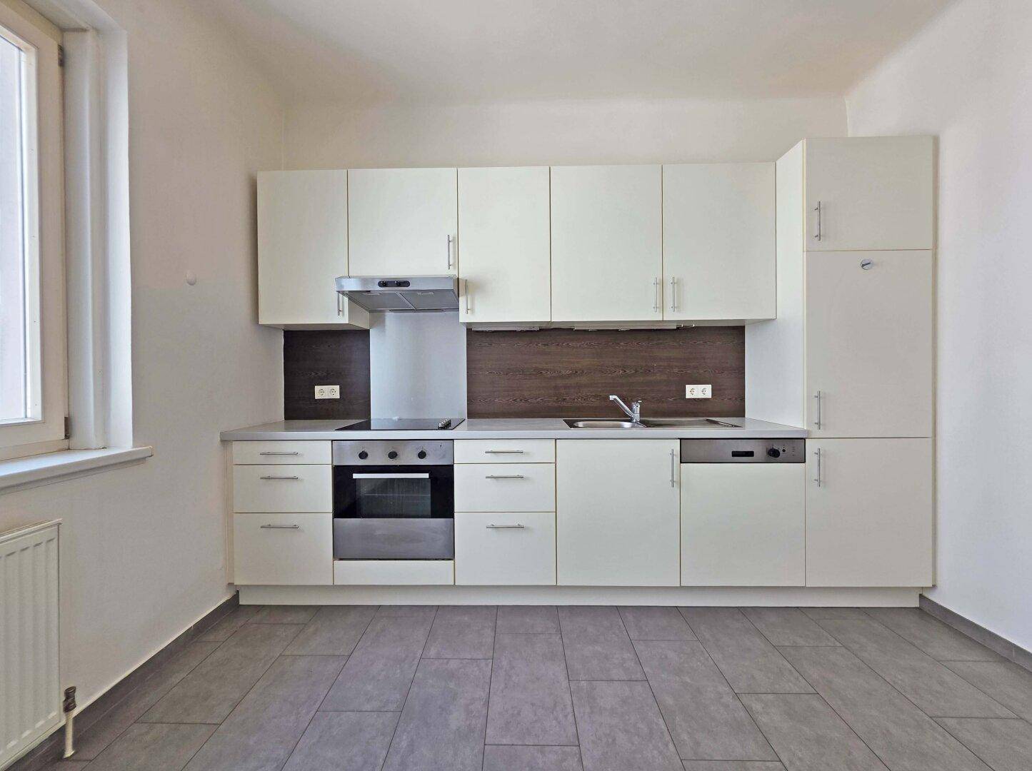 Moderne Einbauküche mit weißen Schränken, integrierten Geräten und Fliesenboden.