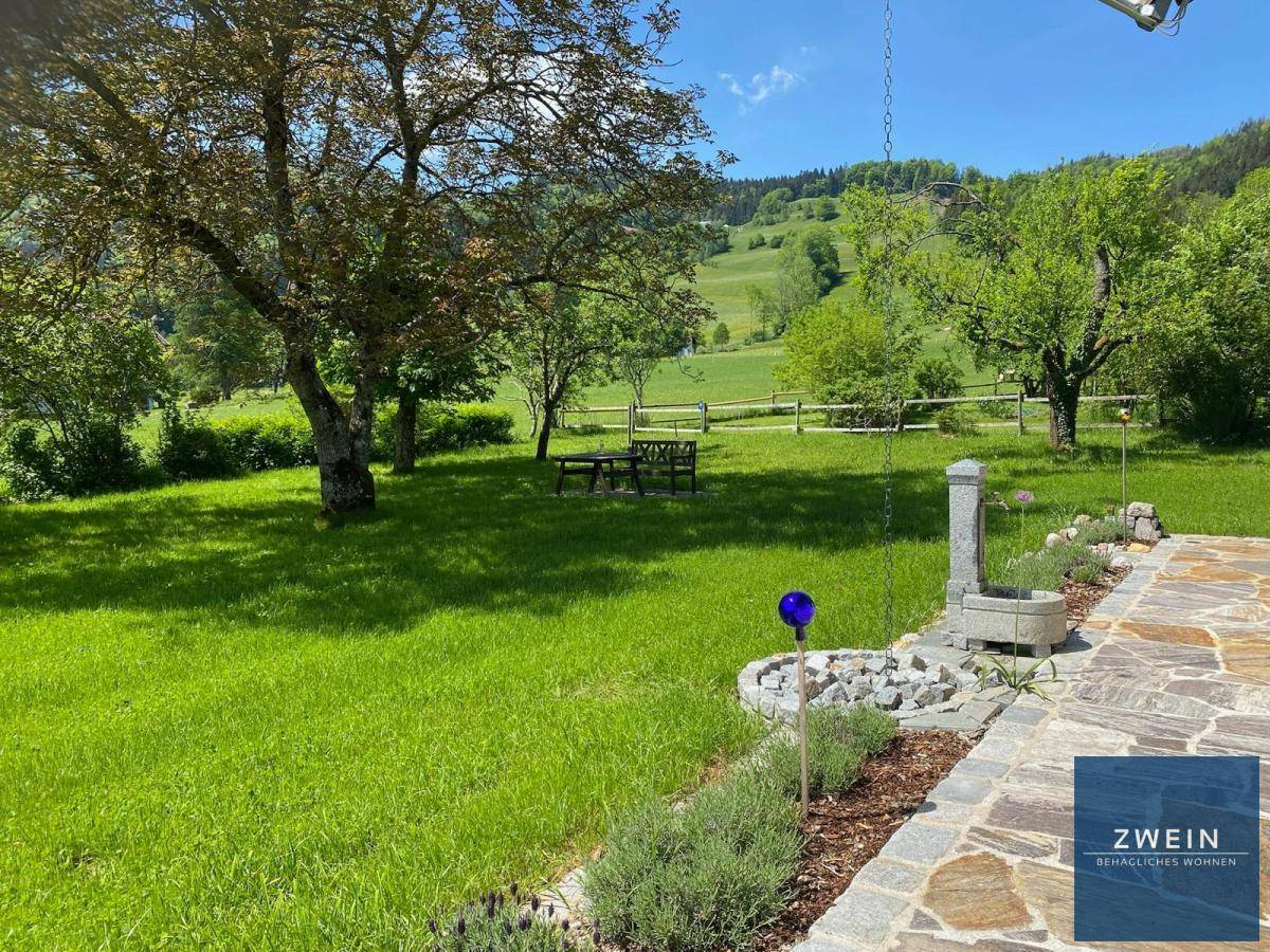 Großer, gepflegter Garten mit Rasenfläche, alten Bäumen und Steinterrasse mit Bergblick.