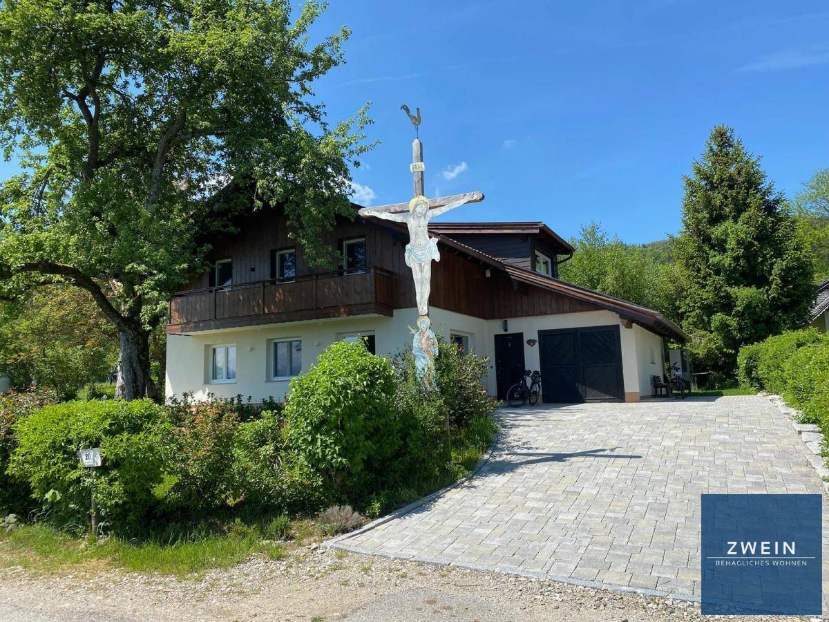 Traditionelles Landhaus mit Garage, gepflasterter Auffahrt und religiöser Skulptur im Vorgarten.