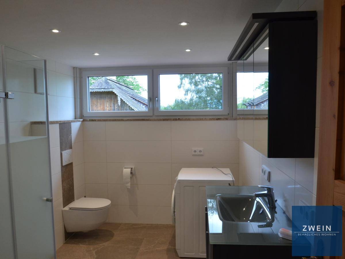 Modernes Badezimmer mit Dusche, wandhängendem WC und Fenster, hell gefliest.