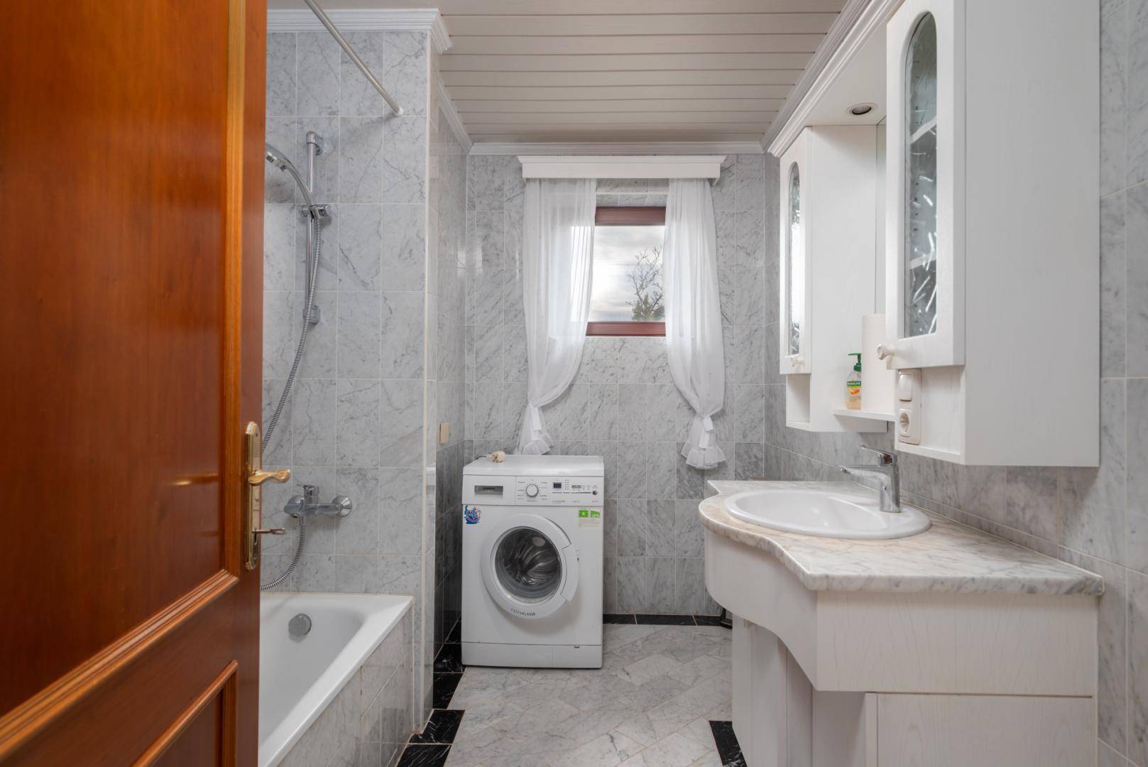 Badezimmer mit Marmorfliesen, Badewanne, Waschmaschine und Einzelwaschbecken.