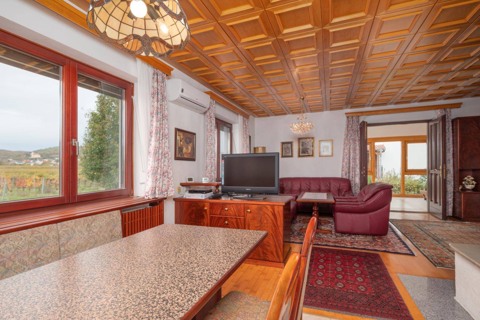 Wohn- und Essbereich mit Holzkassettendecke, Parkettboden und Blick auf die Weinberge.