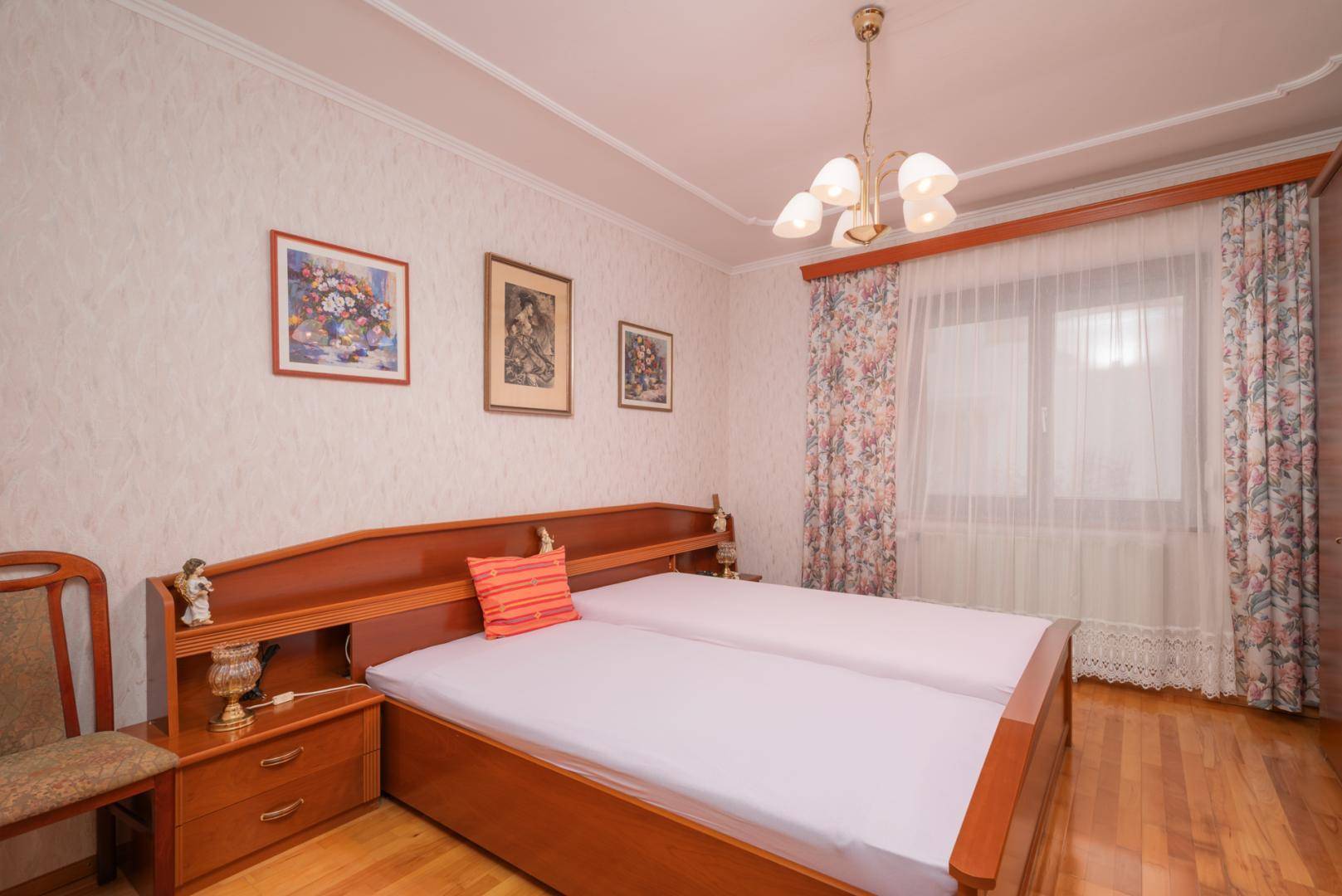 Schlafzimmer mit Parkettboden, floraler Tapete und traditionellem Doppelbett.