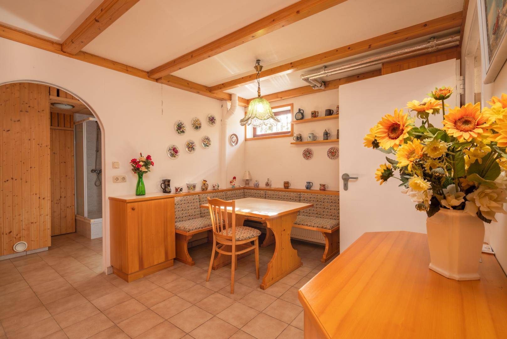 Essbereich mit rustikalen Holzbänken, Fliesenboden und Blick auf den Saunabereich.