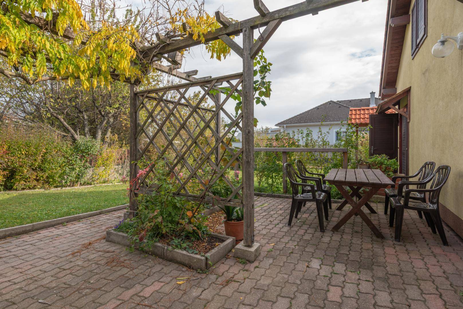 Gepflasterte Terrasse mit Holztisch, Stühlen und einer bewachsenen Pergola im Garten.