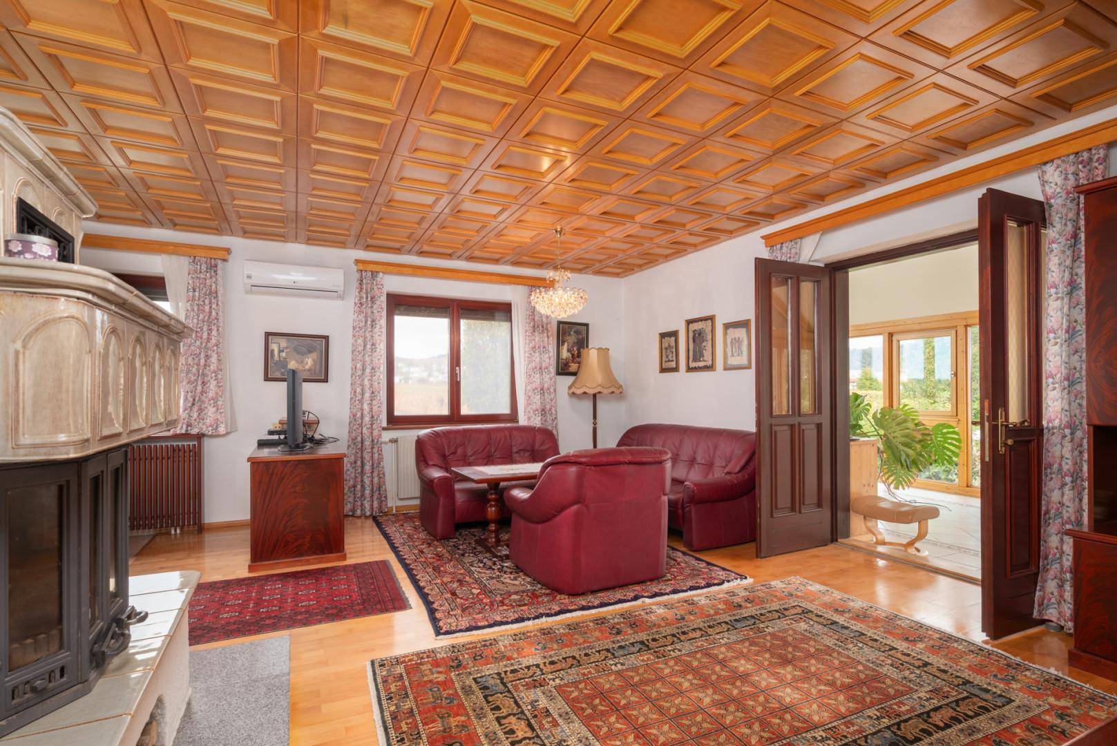 Gemütliches Wohnzimmer mit Kachelofen, Holzkassettendecke und Zugang zum Wintergarten.