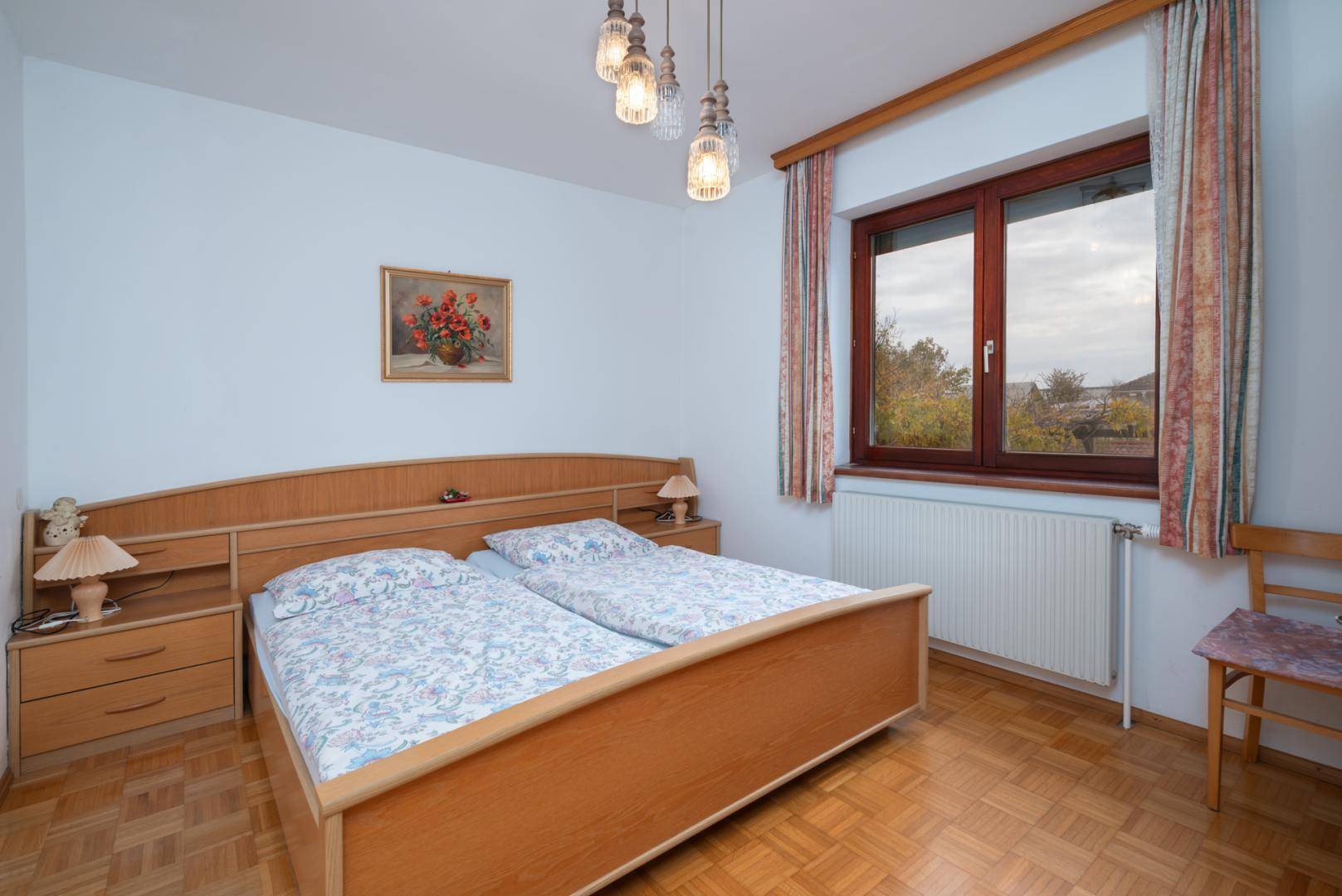 Schlafzimmer mit Parkettboden, Doppelbett und Fenster mit Blick ins Grüne.