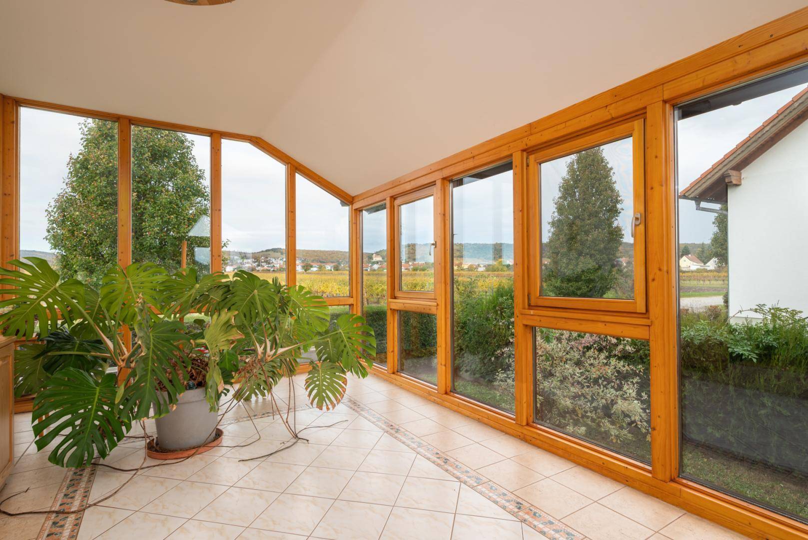 Heller Wintergarten mit großen Fenstern, Fliesenboden und Blick auf die Landschaft.