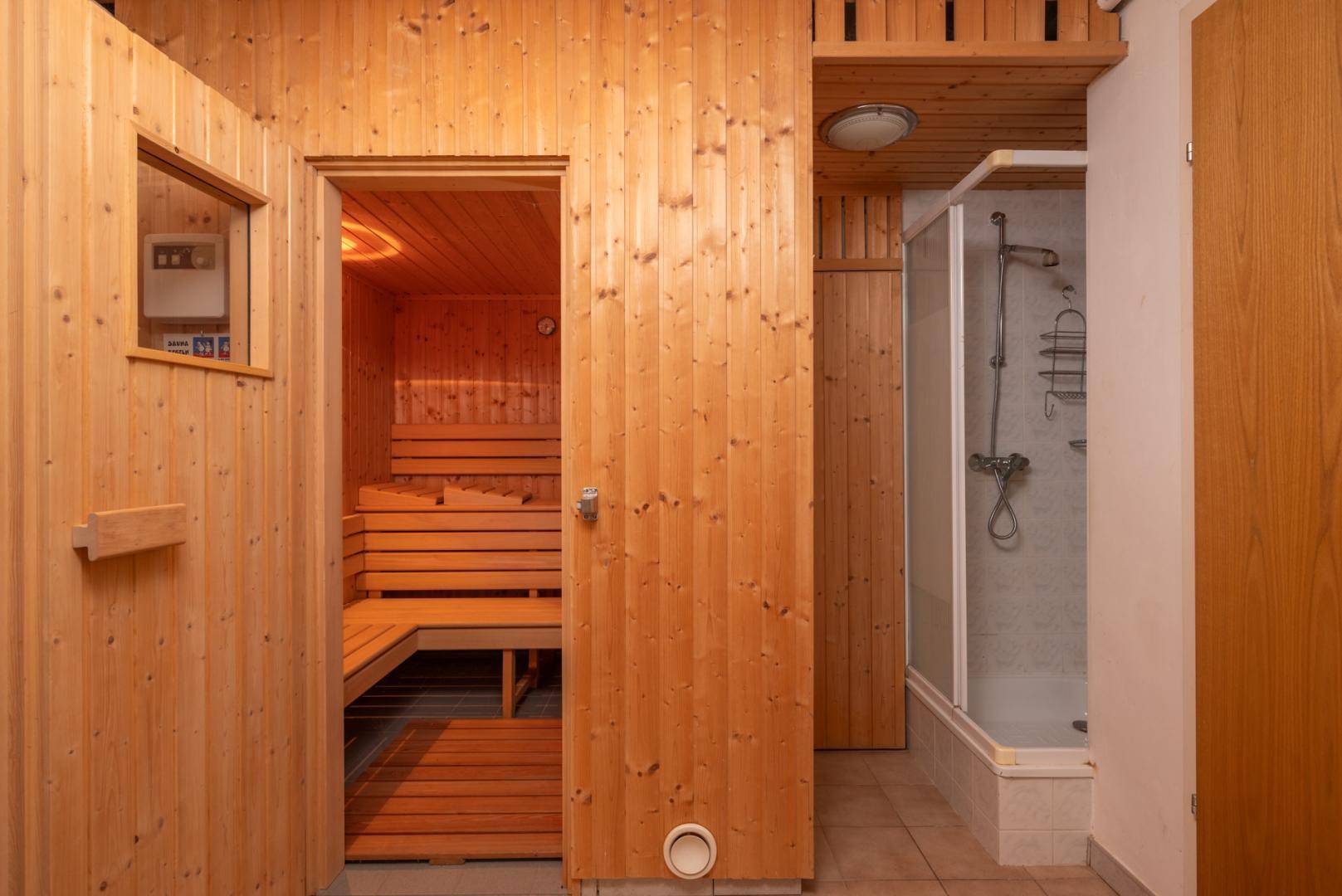 Saunakabine aus Holz mit Bänken und angrenzender Duschkabine.