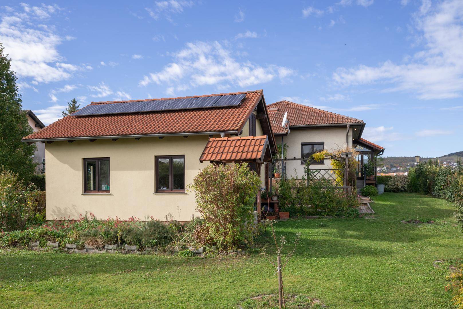 Rückansicht des Hauses vom Garten aus mit Photovoltaikanlage und gepflegter Rasenfläche.