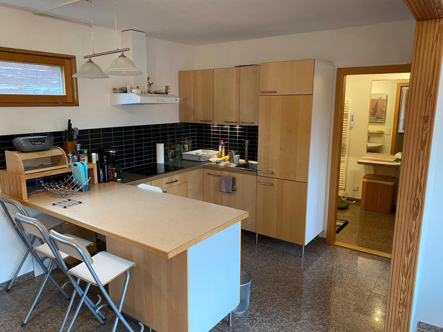 Helle Küche mit Holzschränken, schwarzem Fliesenspiegel und integrierter Kochinsel mit Barhockern.