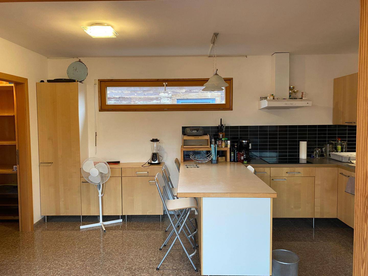 Funktionale Küche mit hellen Holzfronten, Kochinsel und Fenster, gut ausgestattet für den Alltag.