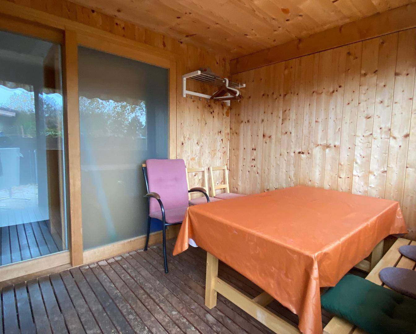 Gemütlicher Wintergarten mit Holzwänden und einem Esstisch, ideal für Mahlzeiten im Grünen.