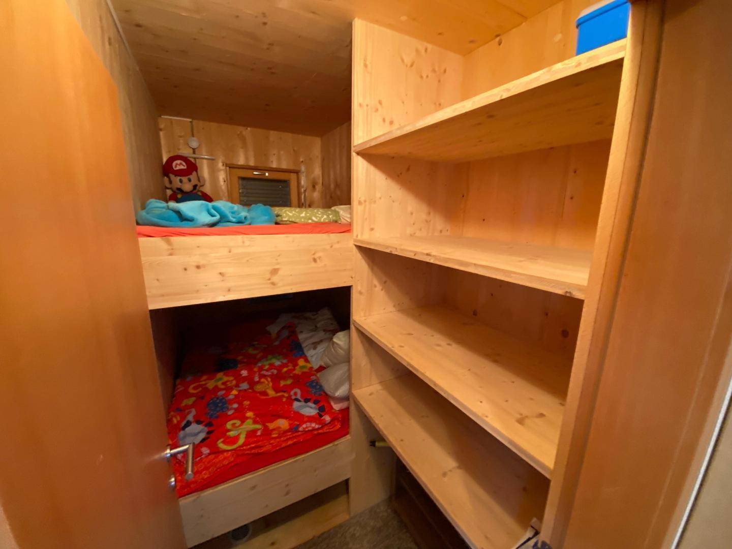 Kompakte Schlafkoje mit Etagenbett und integrierten Holzregalen, ideal für Kinder oder Gäste.