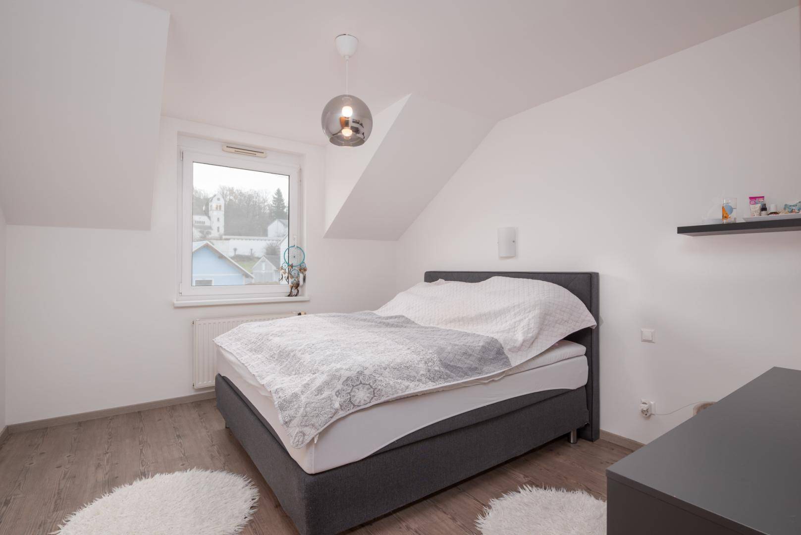 Helles Schlafzimmer im Dachgeschoss mit schrägen Wänden und Laminatboden.