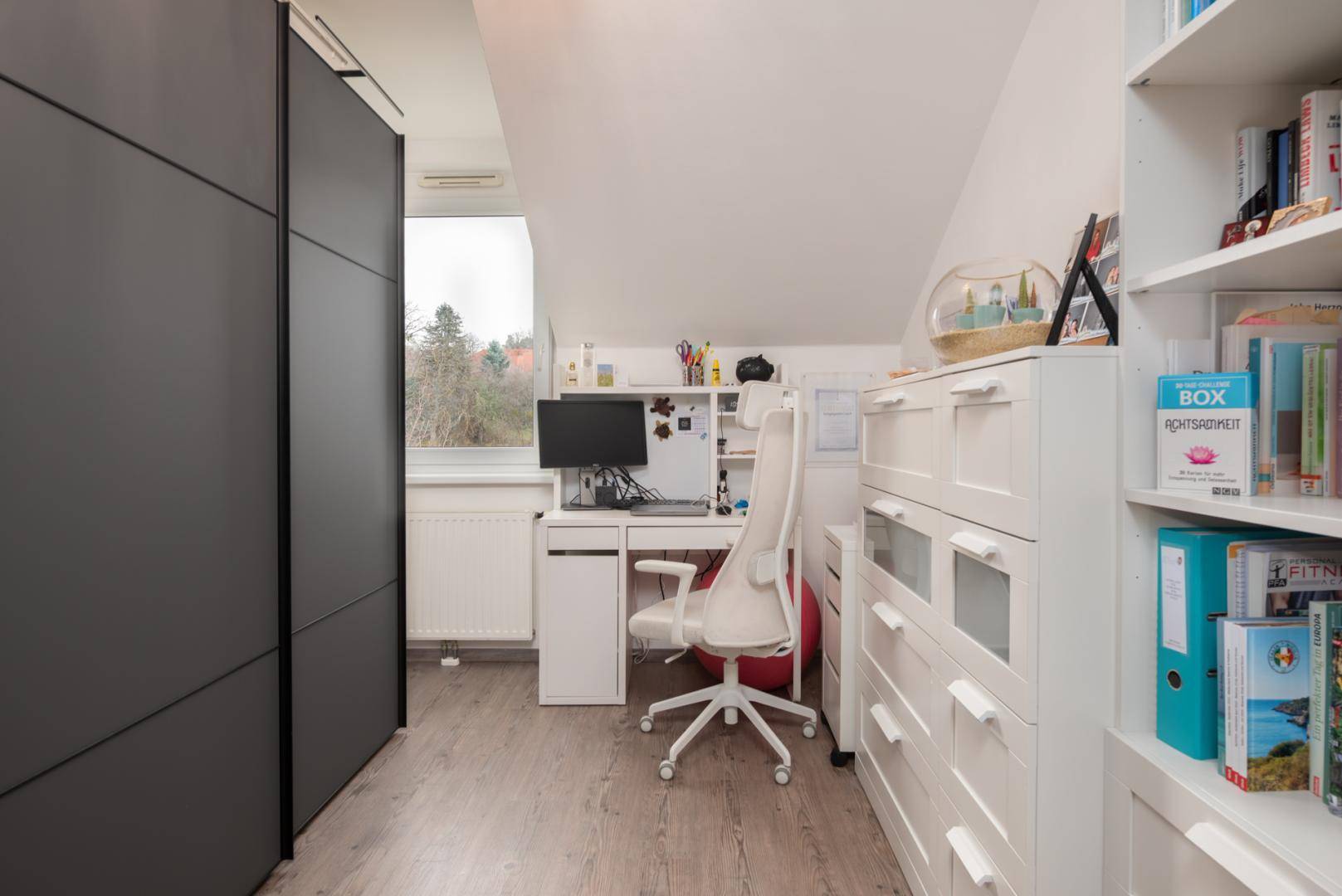 Funktionaler Arbeitsbereich im Dachgeschoss mit Schreibtisch, Regalen und Stauraum.
