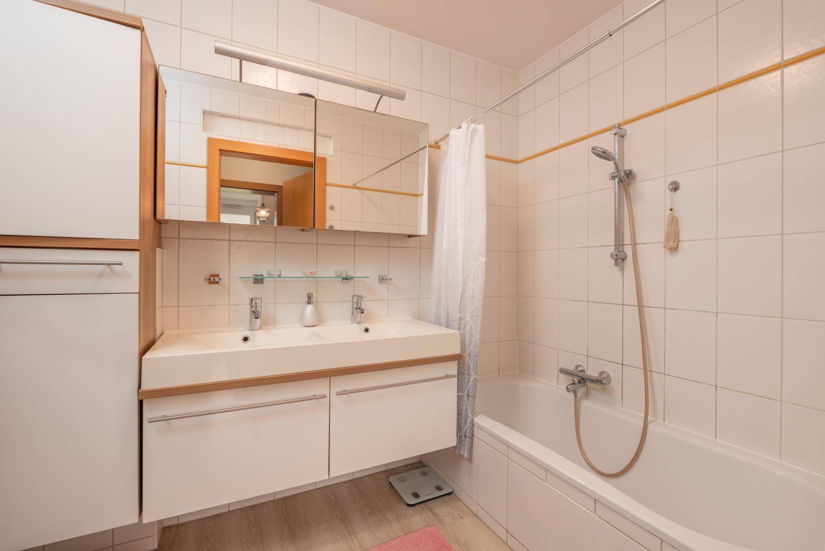 Helles Badezimmer mit Badewanne, Doppelwaschbecken und weißen Fliesen.