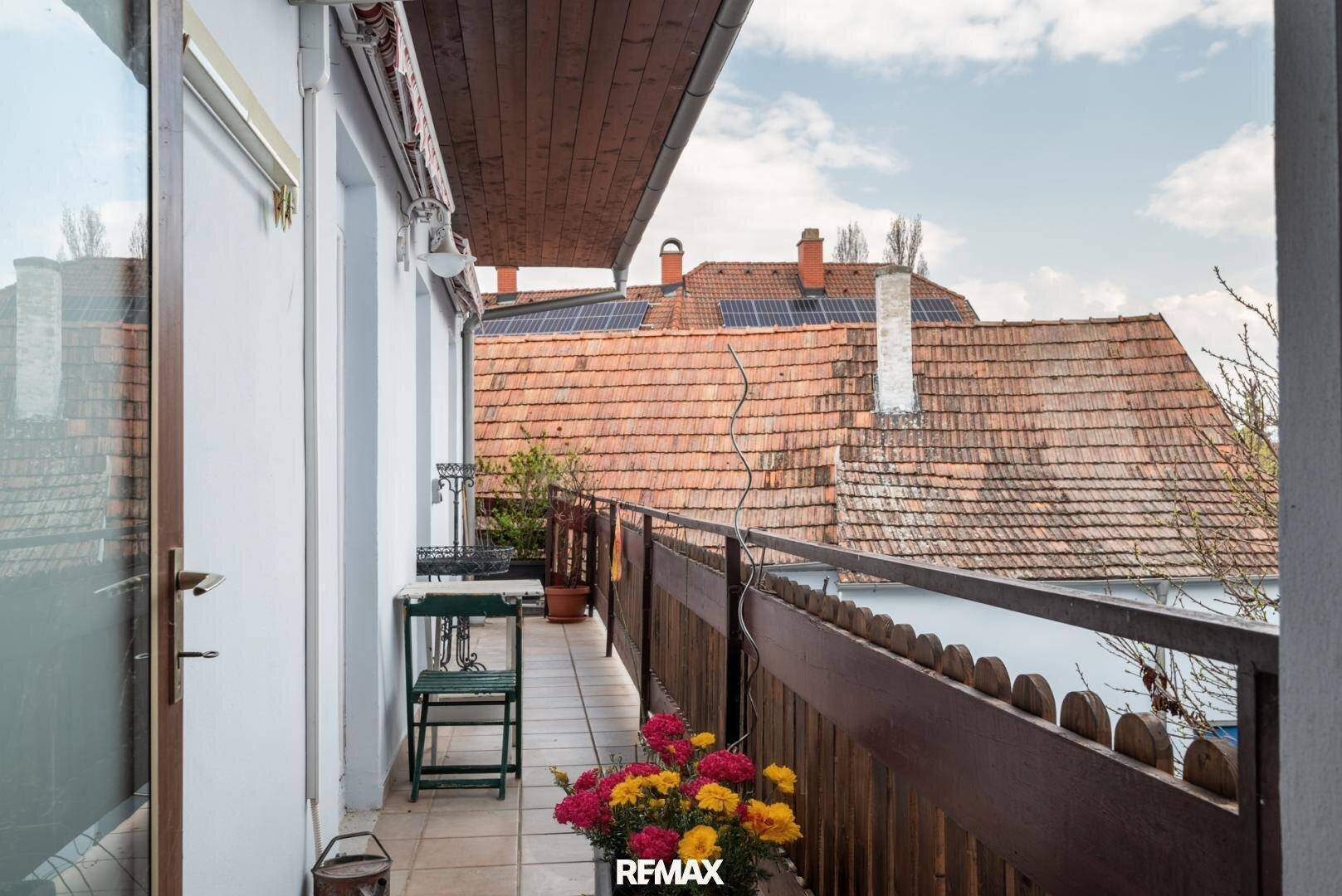 Schmaler Balkon mit Fliesenboden, Blumen und Blick auf die Dächer.