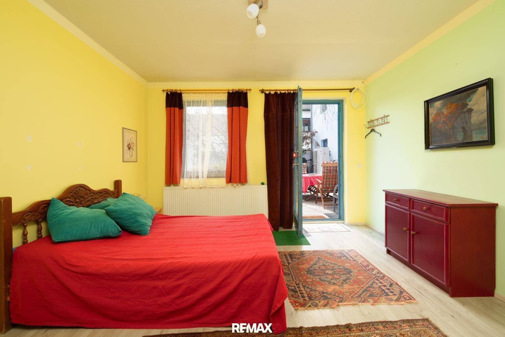 Schlafzimmer mit gelben Wänden, Holzbett und Zugang zur Terrasse.