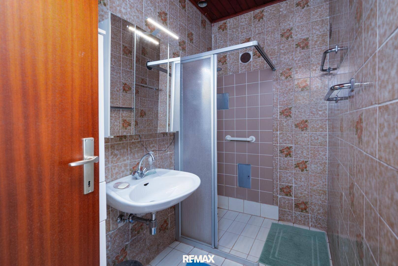 Badezimmer mit Duschkabine, Waschbecken und braunen Fliesen.