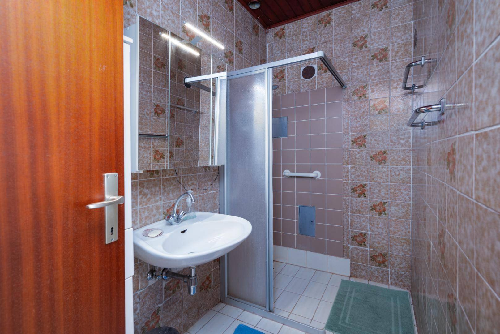 Kleines Badezimmer mit Dusche, Waschbecken und gemusterten Fliesen.
