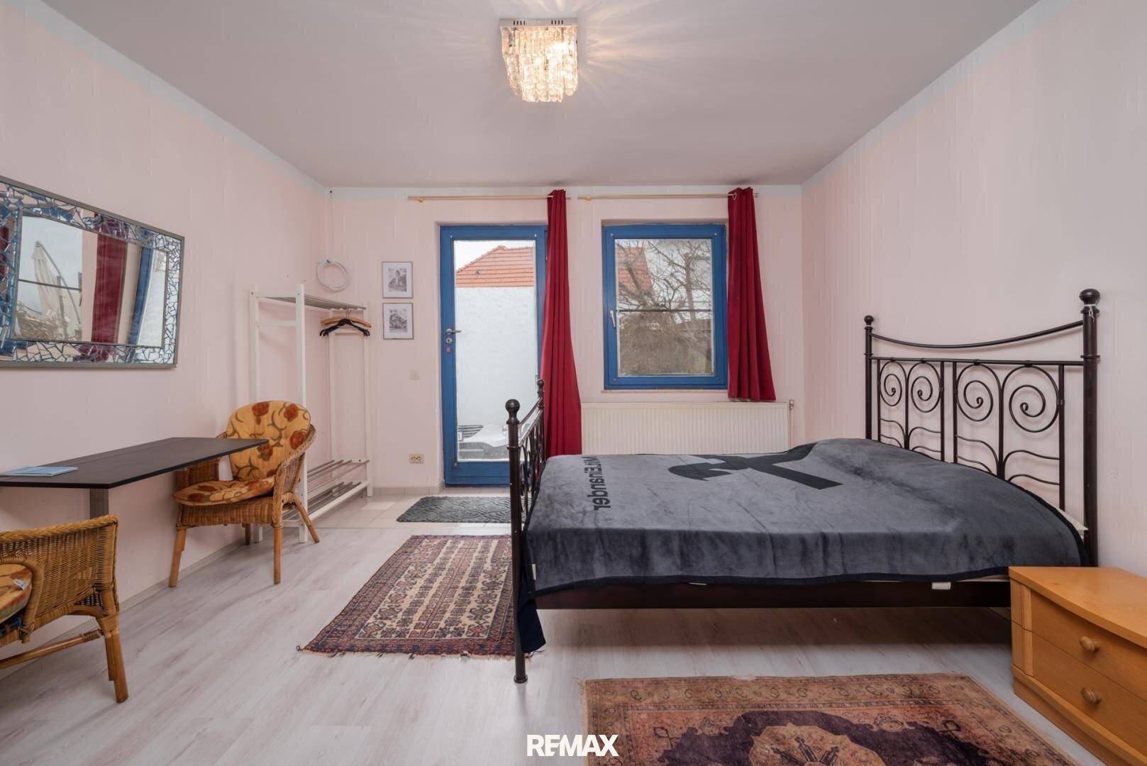 Schlafzimmer mit hellem Boden, Metallbett und Zugang zu einem kleinen Balkon.